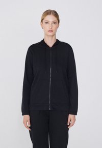 Veste à capuche zippée noire en tissu doux, dotée d'une capuche, de poches avant et de cordons de serrage. Design simple, coupe décontractée et manches longues.
