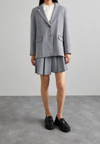 Blazer de pata de gallo, en gris y negro, con dos bolsillos; combinado con una falda plisada a juego; mocasines negros con suelas gruesas.