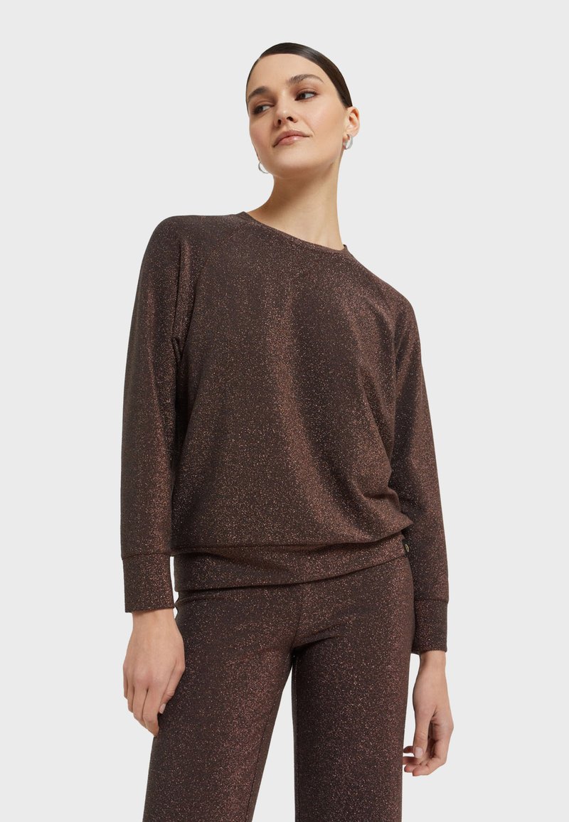 Metalická bronzová mikina s dlouhými rukávy, volným střihem a žebrovanými manžetami. Spárována s odpovídajícími přiléhavými kalhotami pro harmonizovaný vzhled.