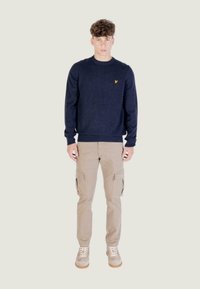 Maglione a maglia blu navy con scollo a girocollo, abbinato a pantaloni cargo beige con tasche laterali e sneakers grigie con suole bianche.