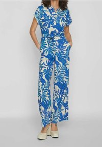 Modrý a bílý květinový overal s krátkým rukávem, předním zapínáním na knoflíky a uvázaným pasem. Má široké nohavice a kapsy.