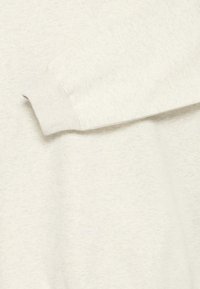 Gros plan d’un sweat-shirt à manches longues couleur blanc cassé montrant un poignet côtelé et un tissu texturé.