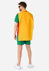 Šarena majica kratkih rukava s žutim plaštem, koja ima crvene i zelene akcentne boje. Nosiva s zelenim kratkim hlačama i bijelim cipelama.