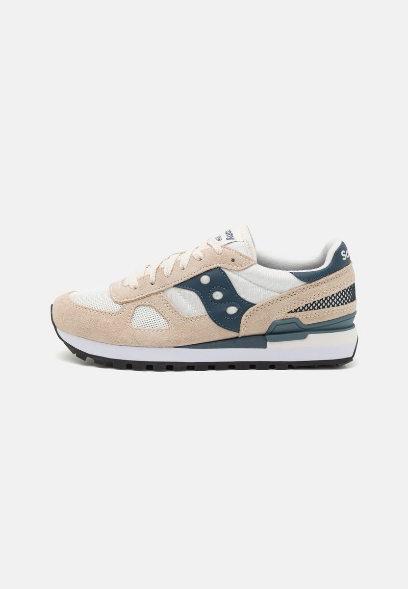 Beige velúr és fehér hálós felsőrésszel rendelkező sneaker, tengerészkék kiegészítőkkel, kerek fűzőkkel és textúrált fekete gumitalppal, fehér középtalppal.