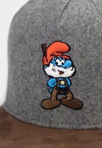 Gray felt cap with a brown suede brim featuring an embroidered Smurf character in blue and red with a brown outfit and a pickaxe.