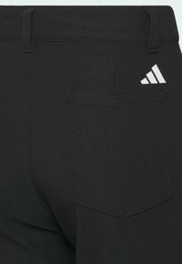 Bolsillo trasero de pantalones negros con logo de Adidas impreso en blanco en la esquina superior derecha del bolsillo.