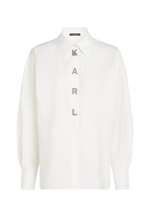 White long-sleeve shirt in lightweight fabric, featuring a classic collar and vertical "KARL" lettering in silver. Cuff detailing visible.