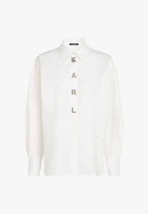 Witte lange mouw hem in lichtgewicht stof, met een klassieke kraag en verticale "KARL" letters in zilver. Manchetdetails zichtbaar.