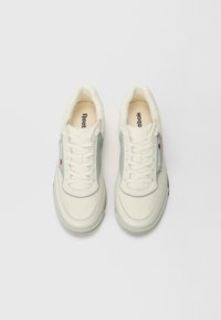 White and light grey sneakers with a smooth leather upper, round toe, lace-up design, and textured rubber sole. Logo on tongue and side panel.