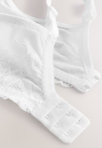 White lace bra with adjustable straps and three-row hook-and-eye closure laid flat on a light surface.