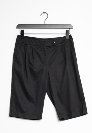 Shorts noirs en tissu léger, dotés d'une fermeture à bouton, de plis à l'avant et de poches latérales. Accrochés à un cintre noir.