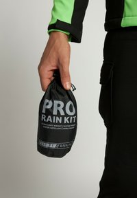 Zwarte, lichte, waterdichte tas met het label "PRO RAIN KIT", met trekkoordsluiting, vastgehouden in een hand, met witte tekst en accenten.