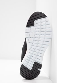 Sulan av en svart och vit Skechers-sneaker lutad mot en vit yta, som visar en texturerad och segmenterad mönster.