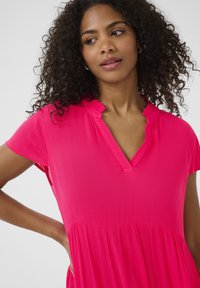 Hot pink dress with a textured finish, features a V-neckline, short sleeves, and a gathered waist for a flowing silhouette.