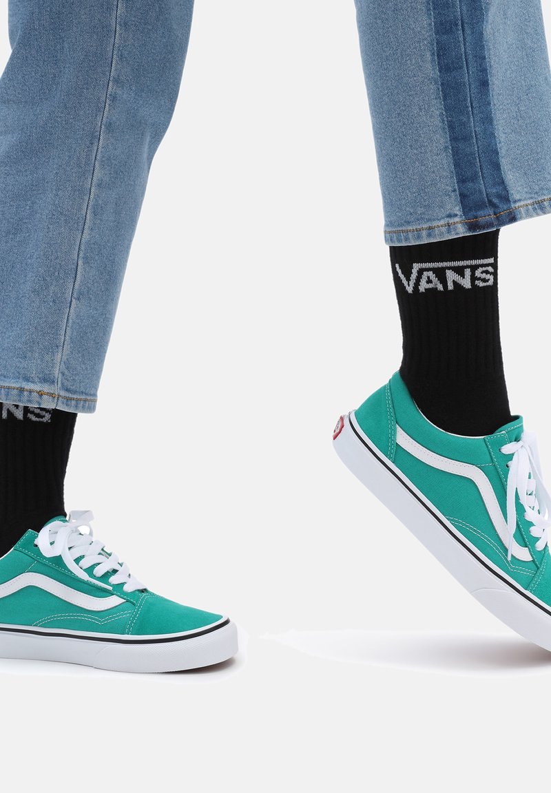 Turquoise canvas sneakers with white accents, black trim, and white laces. Worn with rolled light blue jeans and black Vans logo socks.