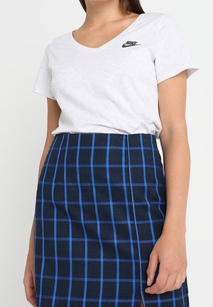 T-shirt blanc à col en V avec logo Nike noir, associé à une jupe à carreaux bleu marine avec des lignes bleues et une fente sur le côté. Texture de tissu lisse.