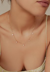 Złoty naszyjnik łańcuszkowy z pięcioma małymi, kwiatowymi akcentami z osadzonymi przezroczystymi kamieniami, na neutralnym tle.