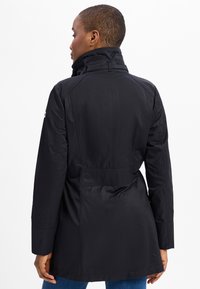 Schwarze Jacke mit hohem Kragen, langen Ärmeln und taillierter Passform. Glattes Material mit strukturierten Nähten und einer Rückenfalte.