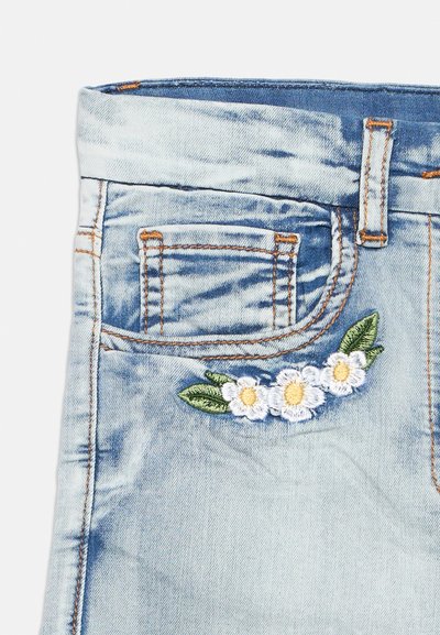 Λεπτομέρεια από ανοιχτό μπλε τζιν παντελόνι με μια μικρή μπροστινή τσέπη και κεντημένα λευκά λουλούδια με πράσινα φύλλα κοντά στην τσέπη.