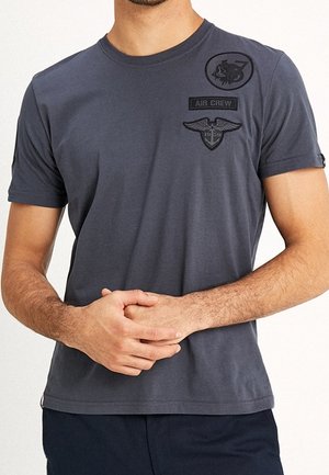 Mørkegrå bomulds-t-shirt med korte ærmer, der har "AIR CREW" og vingerede mærkater på brystet. Glat tekstur.