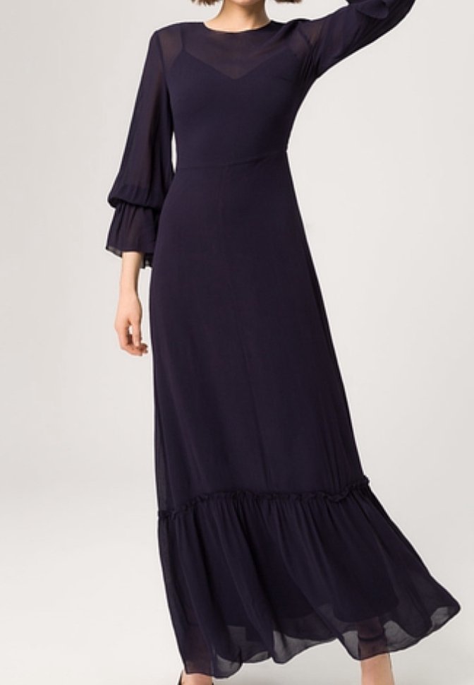 Robe longue navy avec des manches superposées transparentes, un corsage ajusté et un ourlet à volants. Texture lisse avec un léger éclat.