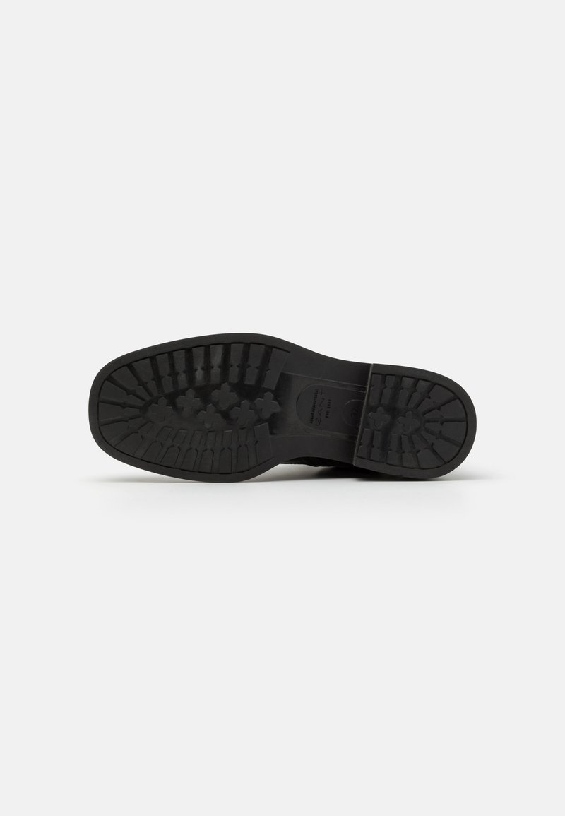 Semelle en caoutchouc noir avec un motif de traction texturé, présentant un bout arrondi et un talon renforcé pour la durabilité et le soutien.