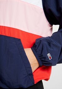 Kurtka przeciwdeszczowa w blokach kolorystycznych, z sekcjami w kolorach granatowym, różowym i czerwonym; lekki materiał nylonowy; elastyczne mankiety; kieszeń z przodu; haftowane logo.