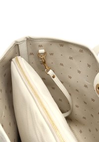 Crème kleurige handtas interieur met zacht, gestructureerd materiaal; gouden rits en hardware; gelabeld lichtbruin patroon op de stofvoering.
