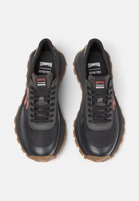 Černé a šedé venkovní boty s gumovou podrážkou, na jazyku s označením "Camper" a "GORE-TEX". Šňůrky jsou pevně utažené.