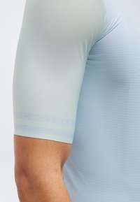 Κοντινό πλάνο στο πάνω μέρος του μπράτσου ενός ατόμου που φοράει ανοιχτόγαλάζιο, υφασμάτινο αθλητικό κοντομάνικο μπλουζάκι.