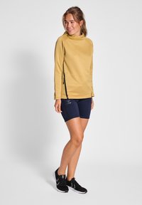 Huvtröja med lång ärm i senapsgul, kombinerad med marinblå shorts. Har sidozipper och svarta detaljer. Svarta sportskor.