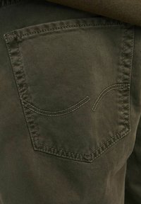 Dark green pants fabric with visible diagonal texture. Back pocket features a curved stitched design. Subtle color variations present.