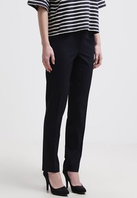 Pantaloni neri su misura con una vestibilità slim e pieghe frontali, abbinati a una maglietta a righe di taglio largo. Texture morbida e linee pulite.