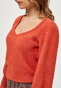 V-Ausschnitt-Pullover in leuchtendem Orange, aus weichem strukturiertem Material gefertigt. Hat lange Ärmel und eine lockere Silhouette.