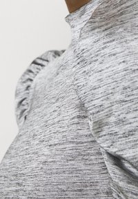 Top grigio testurizzato con collo alto e dettagli sulle spalle a sbuffo, che mostra un motivo maculato e un tessuto morbido.