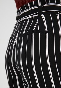 Černobílé pruhované kalhoty s teksturovanou tkaninou, mají přiléhavý pas, poutka na opasek a detail zadní kapsy.