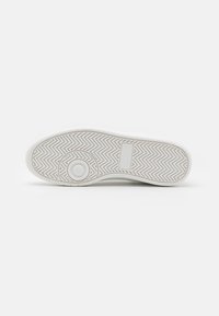 Sole of white sneaker with herringbone tread, circular pivot point near toe, and rectangular patch near heel on plain white background.