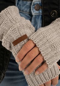 Lichtgrijze gebreide vingerloze handschoenen met ribbelstructuur en een bruine leren label, met een losse pasvorm rond de pols.