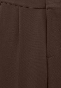 Tissu marron avec une texture lisse, comportant des plis et une poche latérale. Le matériau semble robuste et léger.