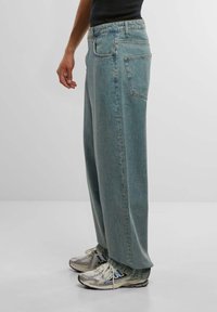 Støveblå vide jeans laget av denim, med høy midje, fem lommer og synlig søm. Kombinert med sølvfargede joggesko.