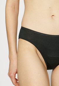 Black ribbed bikini bottom featuring a low-rise waistband and smooth texture. Side coverage with minimal fabric for a streamlined fit.