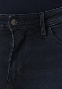 Dark blue denim jeans featuring a straight fit, subtle stitching, and a metal button closure with a brand logo on the waistband.