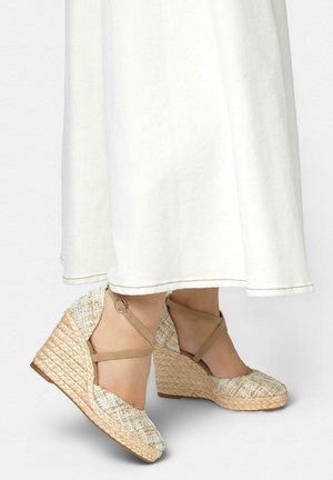 Zapatos espadrilles de cuña tejidos con tiras en el tobillo, usados con una falda larga blanca, que muestran tela texturizada y detalle de tacón trenzado.