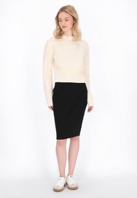 Pulover crem cu umeri texturat, asortat cu o fustă tip creion neagră mulată. Modelul poartă adidași albi cu talpă de un maro deschis.