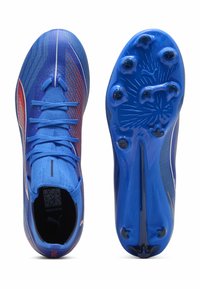 Des chaussures de football synthétiques bleues présentent une tige texturée, des accents rouges contrastants et une semelle à crampons pour la traction. Système de laçage inclus.