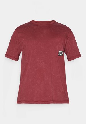 Rød bomulds t-shirt med rund hals, korte ærmer og en struktureret overflade. Har et lille sort og hvidt logo-patch på fronten.