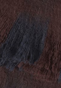 Gros plan sur un tissu doux et duveteux avec des taches brun foncé et noires et une surface texturée, semblable à de la laine.