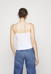 Valkoinen puuvillainen hihaton paita, jossa on ohuet hihnat, muotoiltu malli ja sileä pinta, yhdistettynä korkeavyötäröisiin sinisiin farkkuihin.