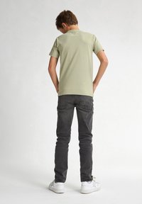 Lichtgroene t-shirt met korte mouwen, gecombineerd met donkergrijze jeans. Casual pasvorm, met witte sneakers. Stikseldetails op de jeans zichtbaar vanaf de achterkant.
