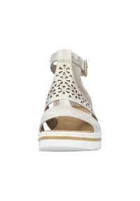 Beige suede sandal with decorative cutouts, ankle strap, gold buckle, and white sole. Flat, open-toe design suitable for warm weather.